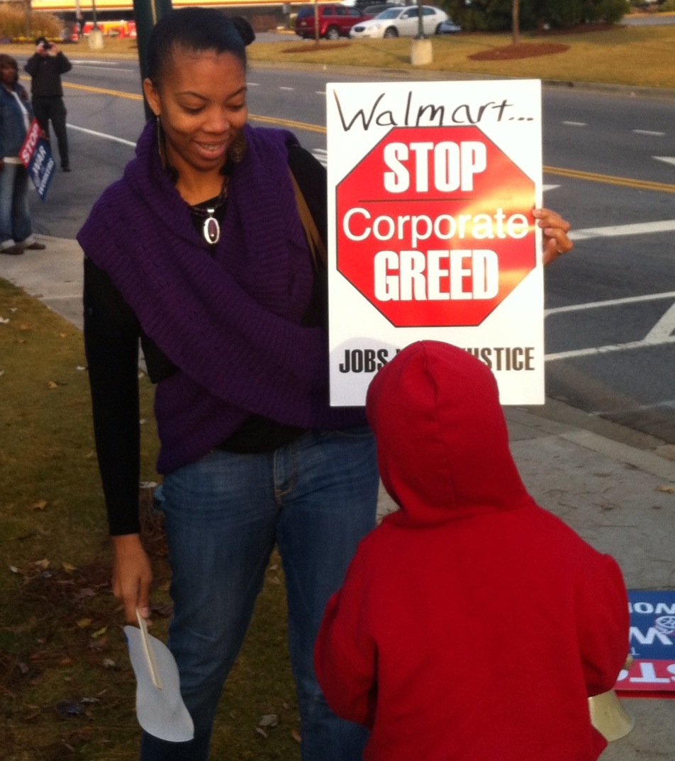 Sheri Davis-Faulkner at a Walmart Action with a Stop Corporate Greed Sign and her son
